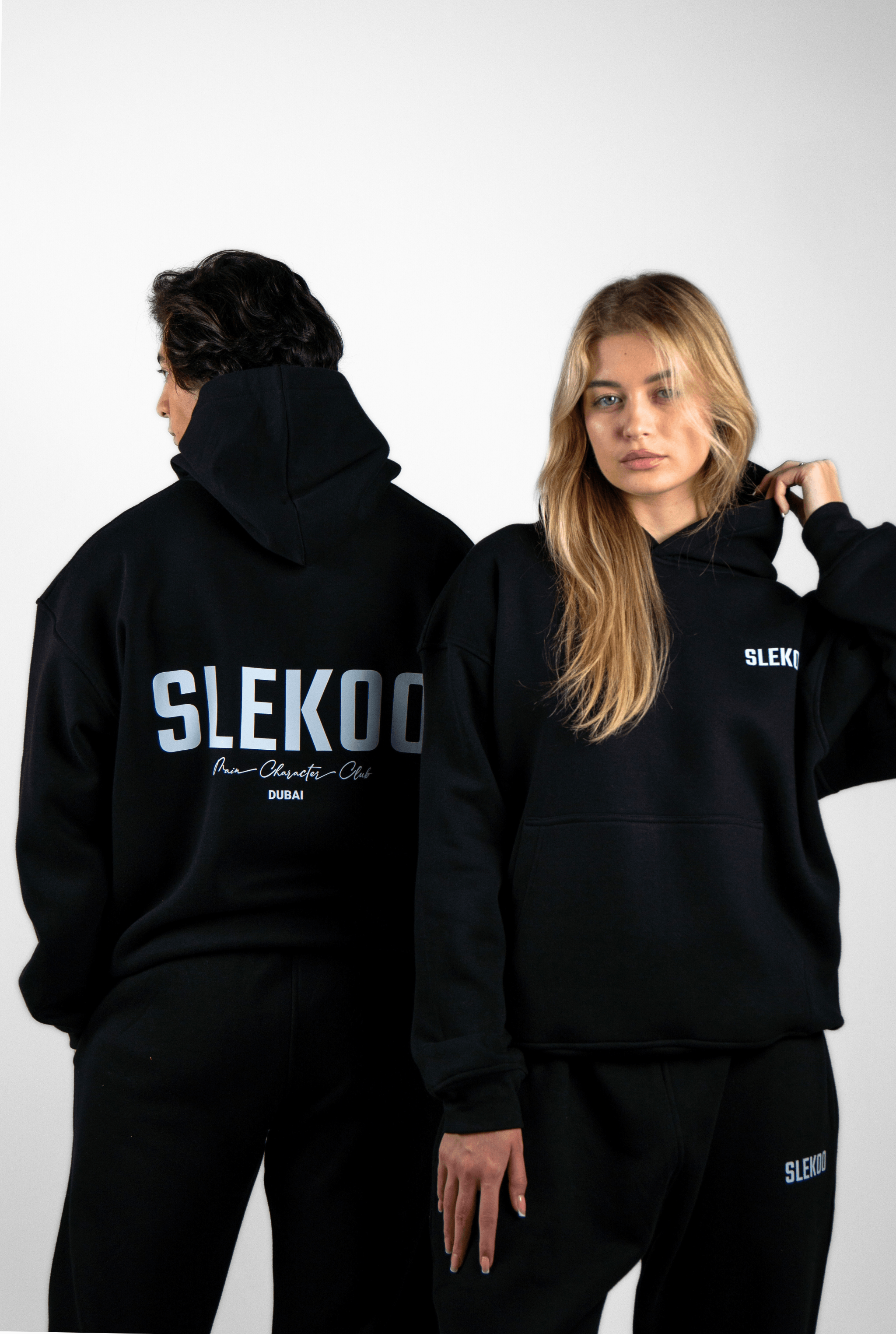 Two models in black hoodies and sweatpants with SLEKOO logo on a white background