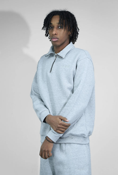 Man wearing light grey quarter-zip sweatshirt and matching sweatpants in minimal studio